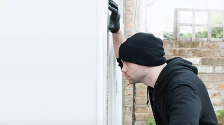 Einbrecher schaut durchs Fenster in die Wohnung rein
